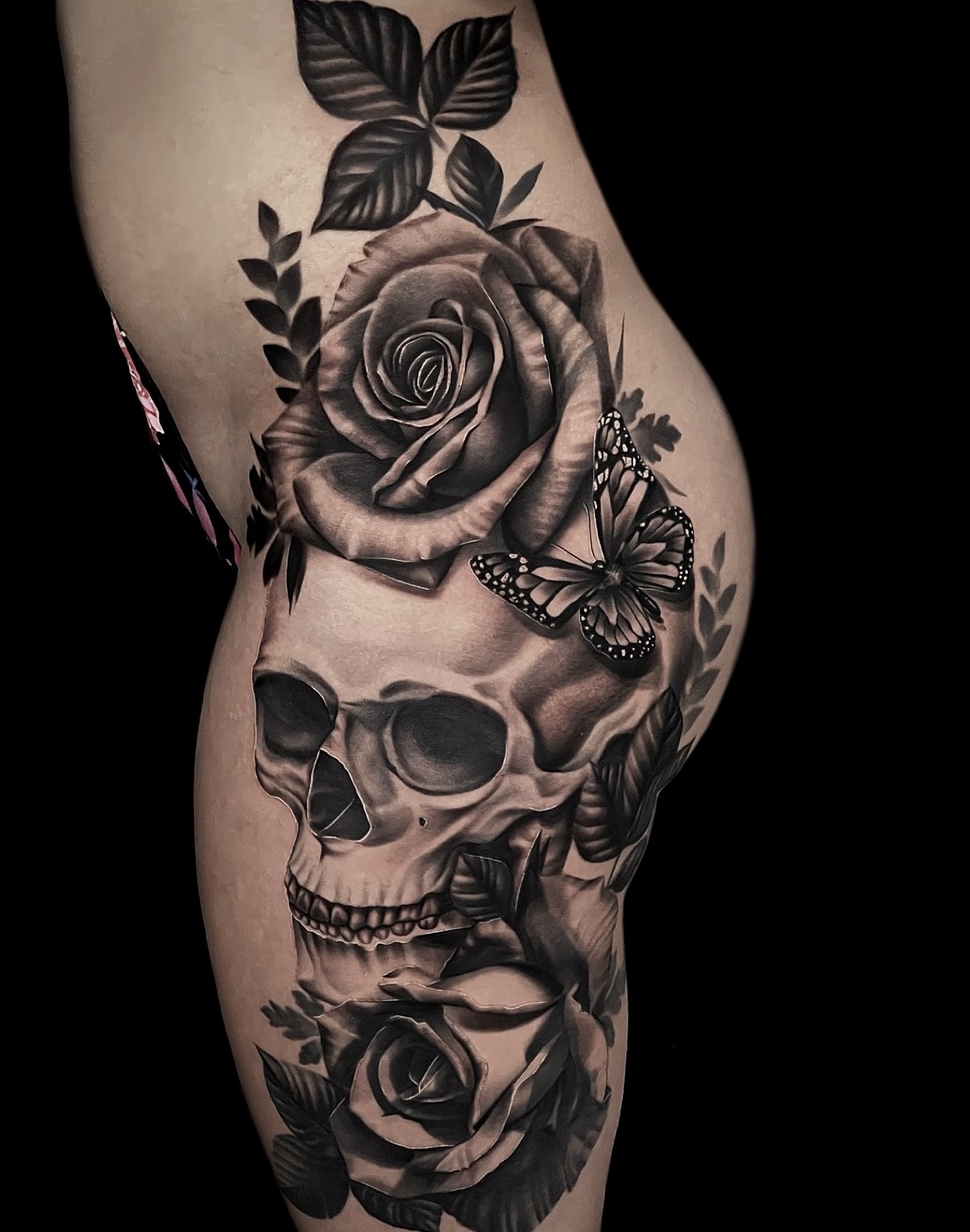 Detailed skull, rose, and butterfly thigh tattoo
